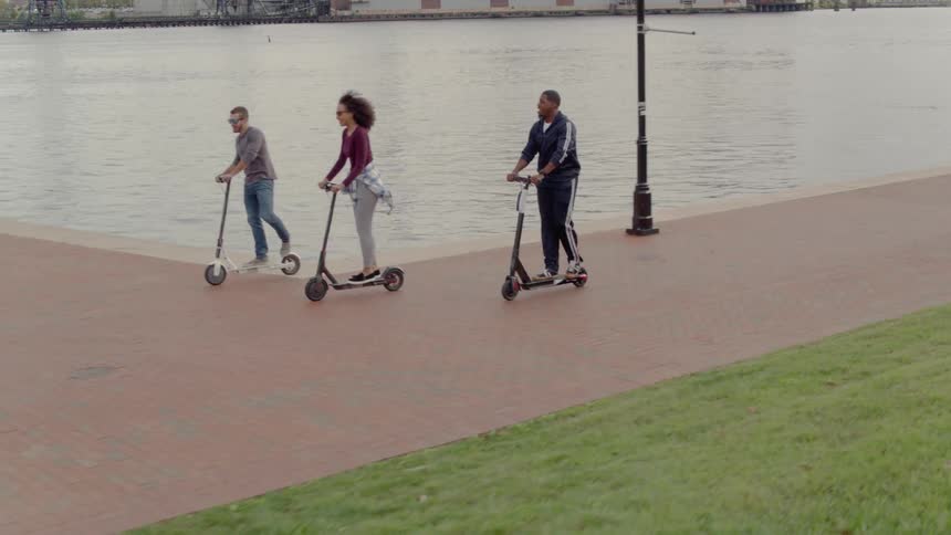 Friends ride scooters on a pier at sunset