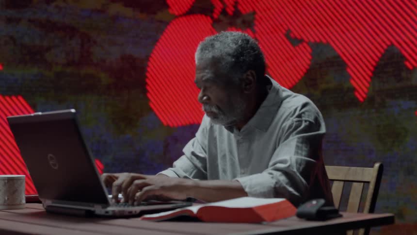 An older man working on computer in front of LED wall