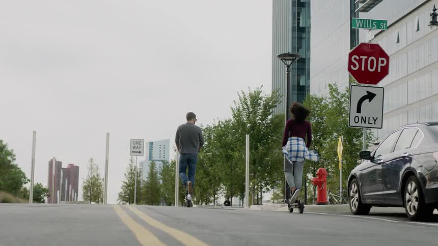 Two people are riding scooters on a city street