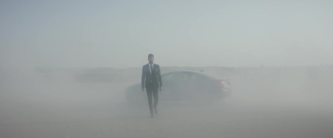 A man is walking away from a car during a sandstorm in a desert landscape
