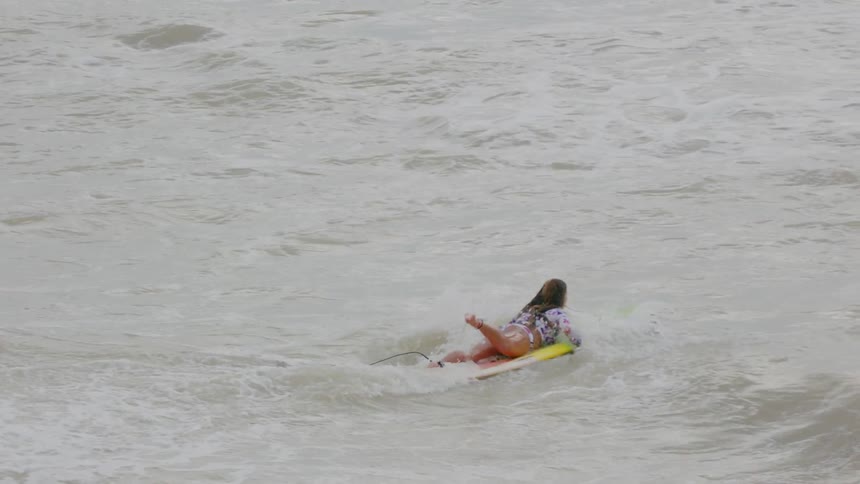 A woman jumps on her surfboard in the ocean