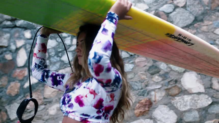 A woman is carrying her surfboard on top of her head