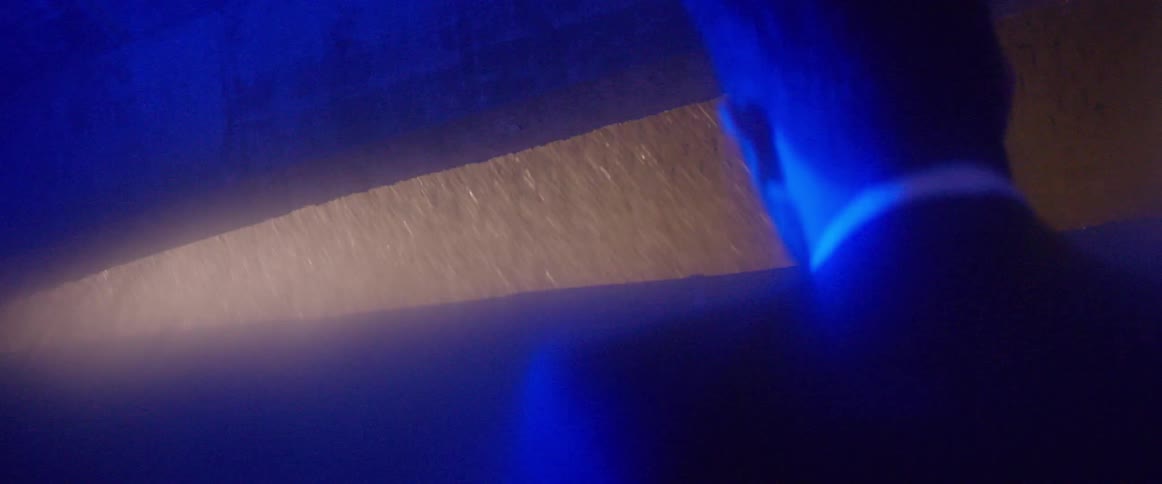 Man bathed in blue light watches rainfall outside