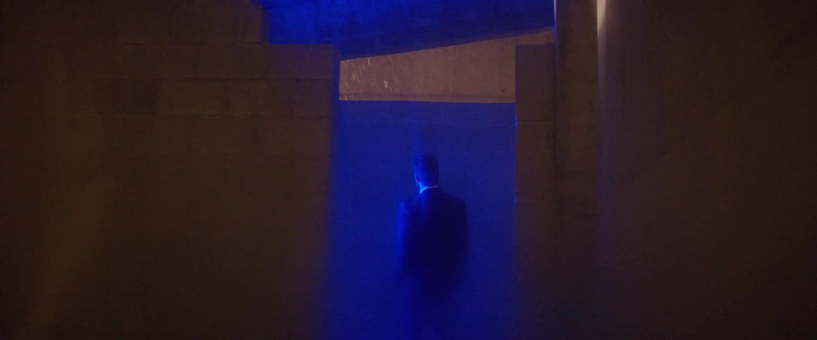 A man stands in a blue light as he looks at the rain