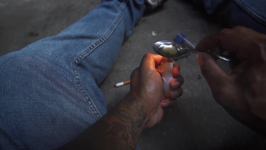 A man is using a lighter to heat up a spoon of possible drugs