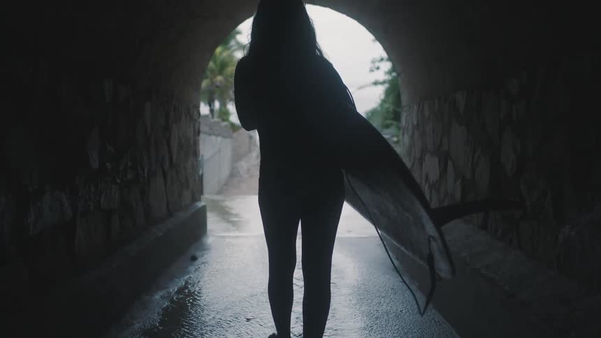 Woman carrying surfboard through a tunnel