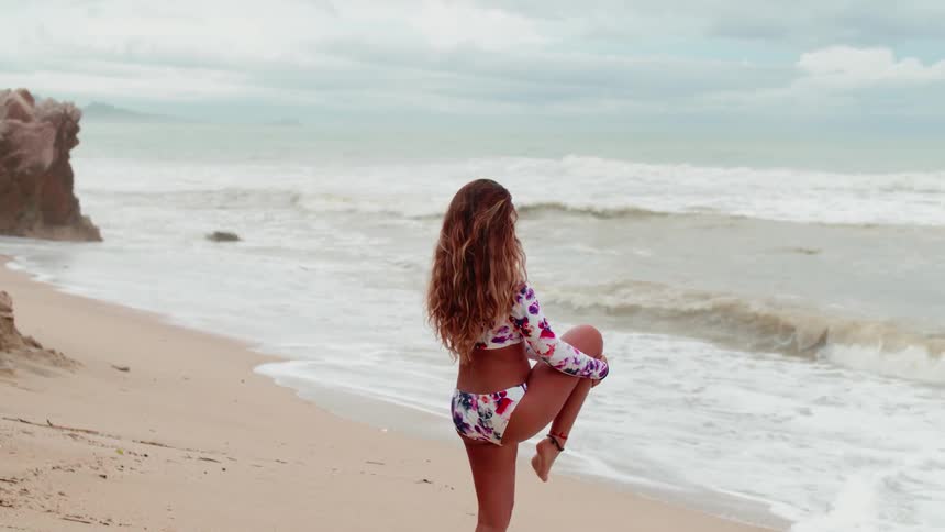 A woman stretches on a sandy beach