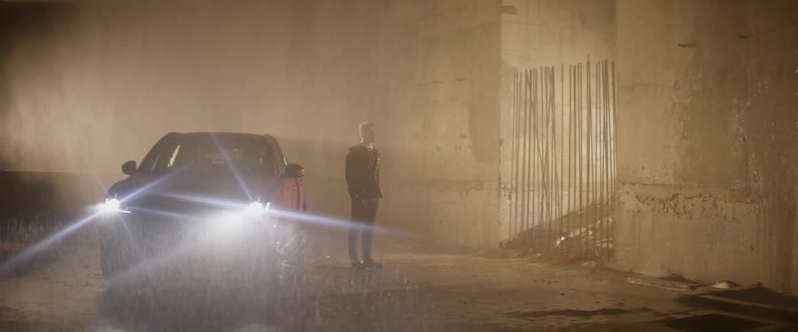 Man stands next to a parked car during a rainstorm