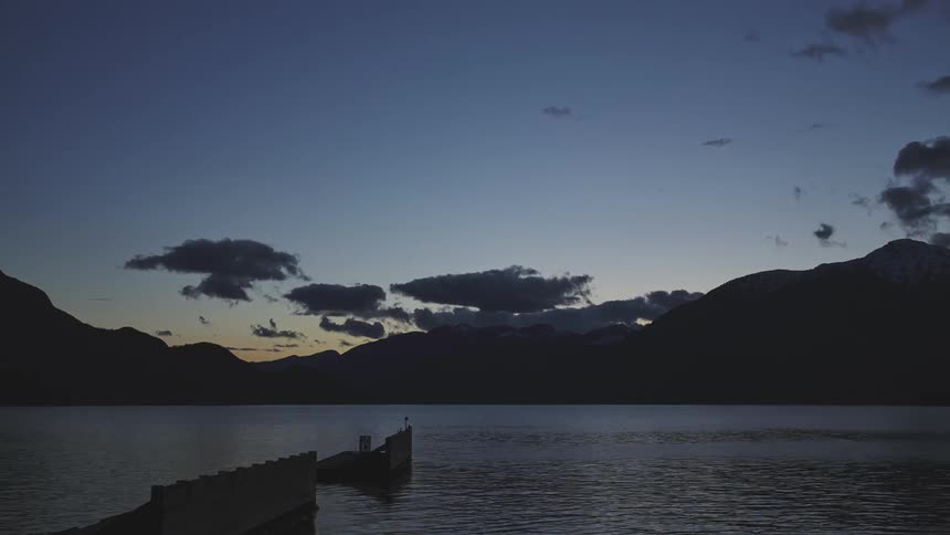 Clouds move across a darkening sky over mountains and a lake