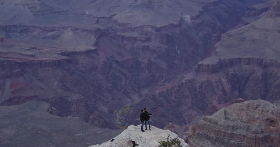 Two people standing on a boulder in the mountains on a cold, overcast day