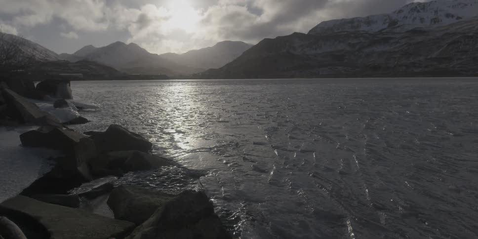 A frozen lake at the base of a snowy mountain