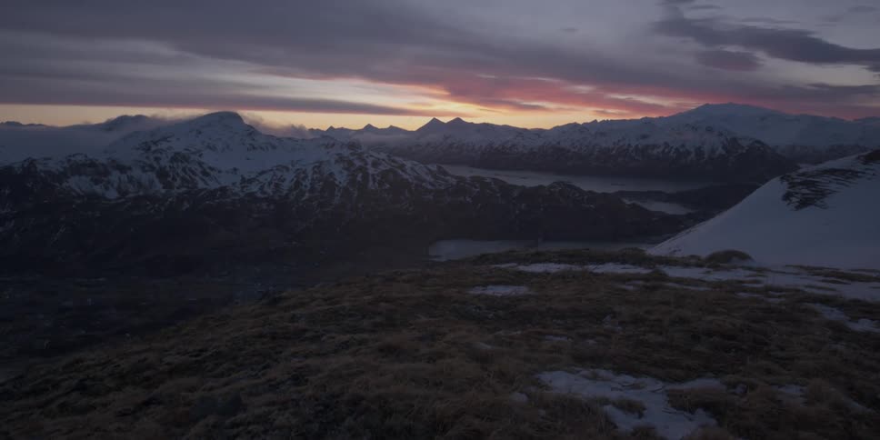 The sun sets behind jagged snowy mountains