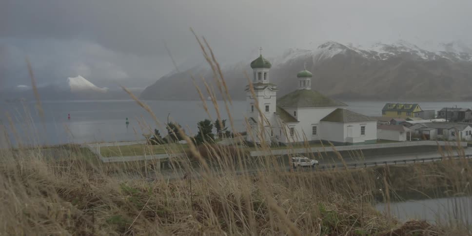 A grassy hill overlooks a church on the shore