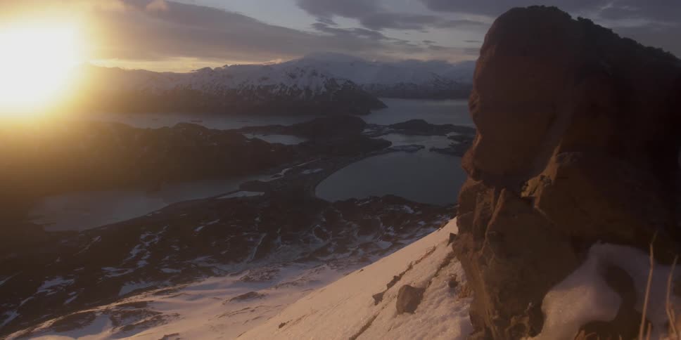 The sun is setting on a frozen coastal mountain