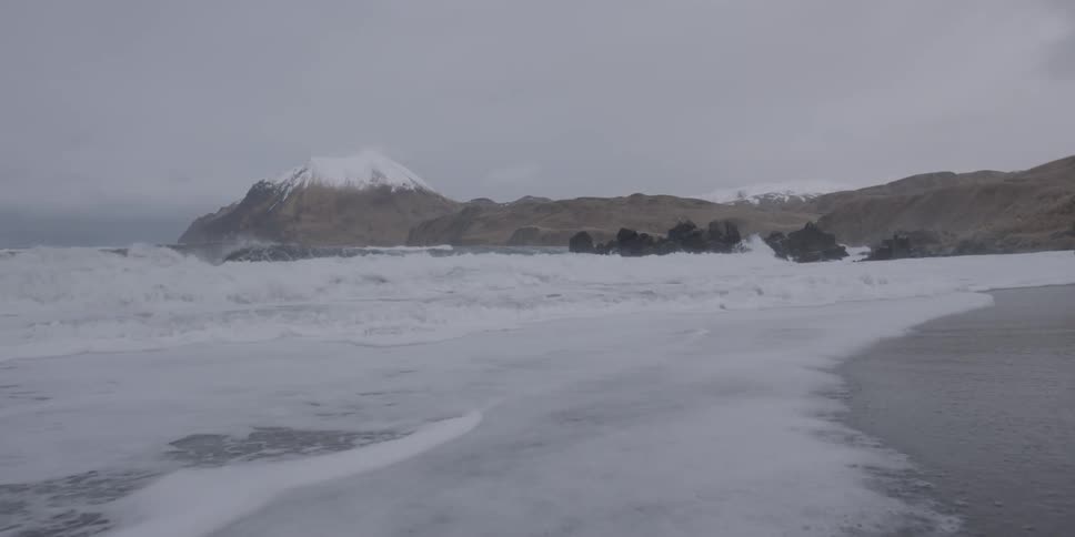 Waves rolling onto a beach near a mountain