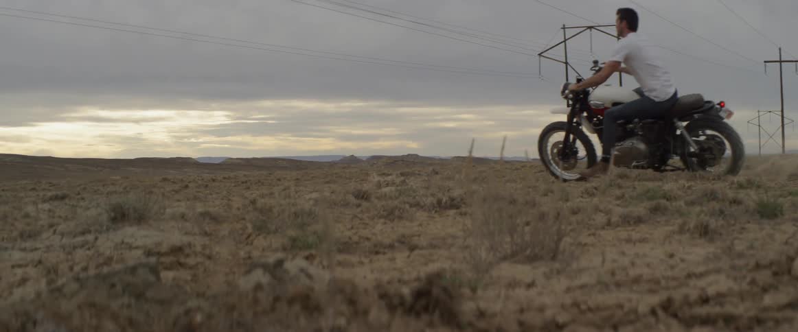 A man riding a motorcycle in the desert kicks up dirt