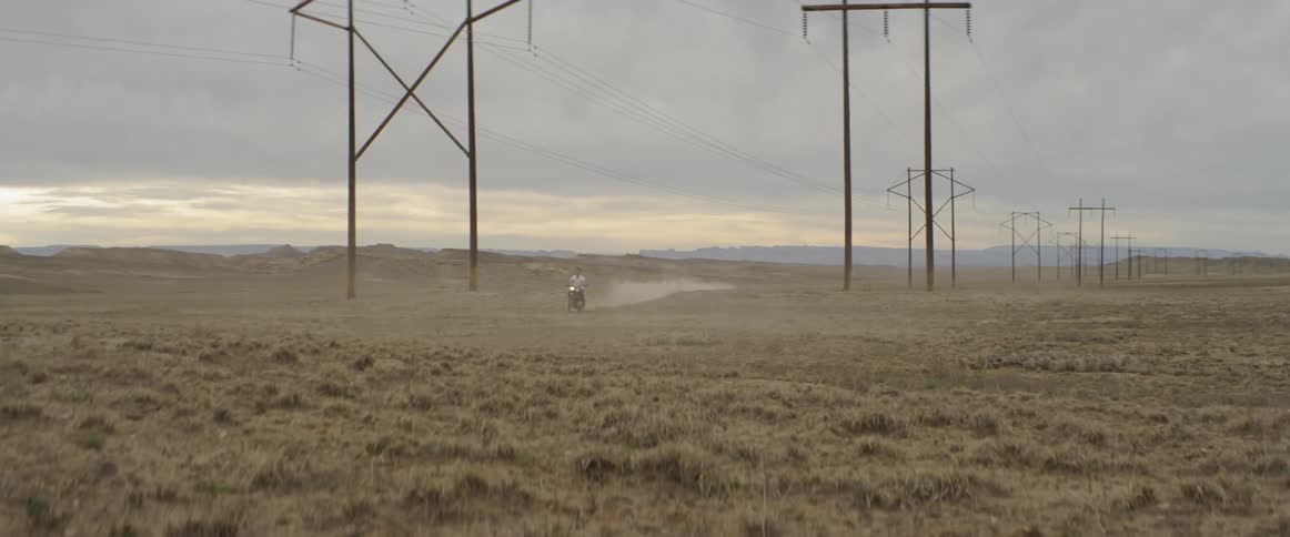 A man rides a motorcycle in a rural field at sunset