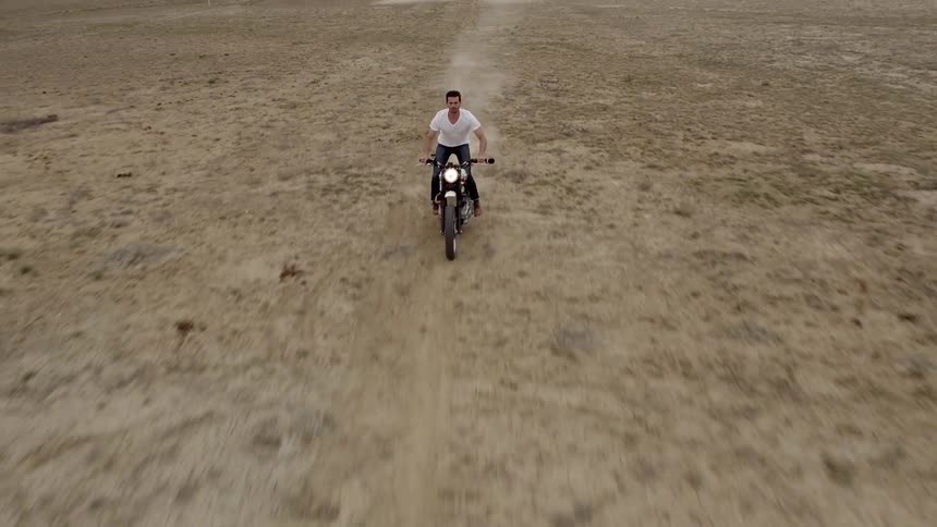 A man drives a motorcycle down a scrubby stretch of desert