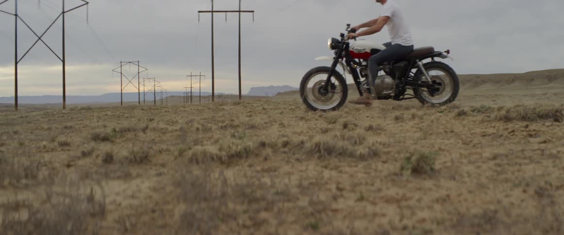 Man riding a motorcycle across a field on a cloudy day