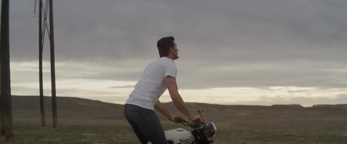 A man rides a motorcycle in a rural field at sunset