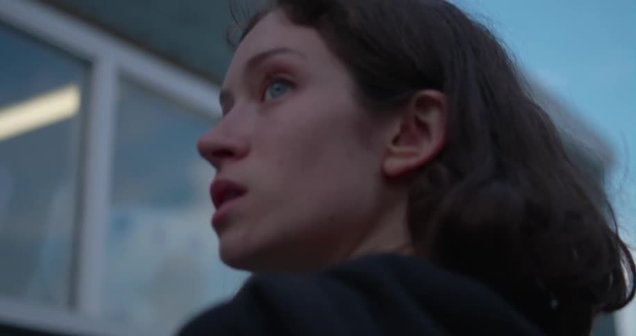 A woman stands next to a building and looks over her shoulder