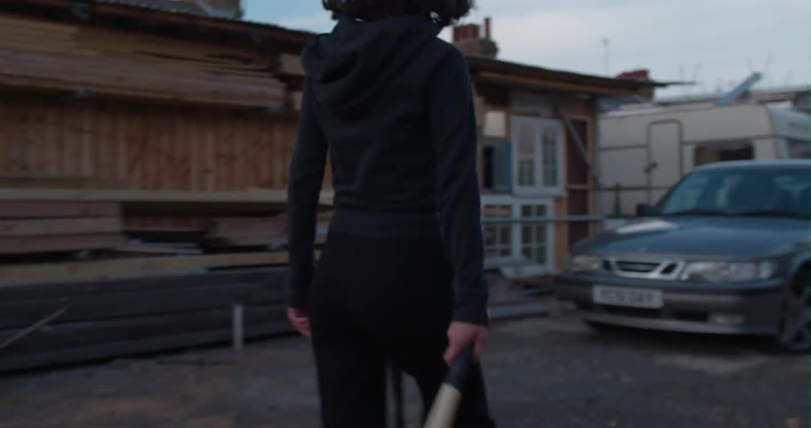 A woman approaches a car with a baseball bat in hand