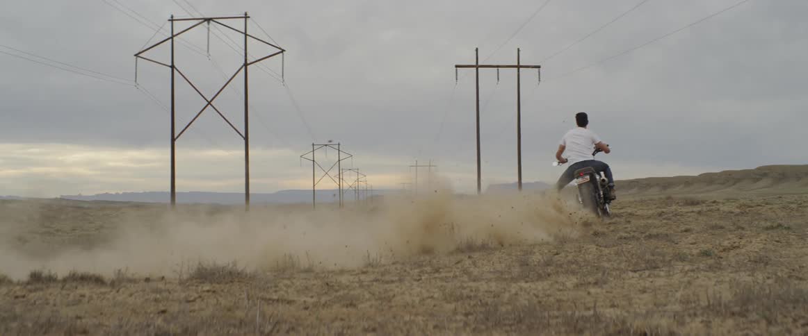 A motorcyclist kicks up dust while riding in a rural field at sunset