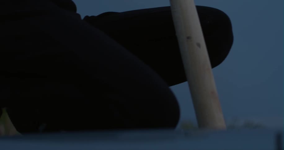 A woman sits with a baseball bat outside at night
