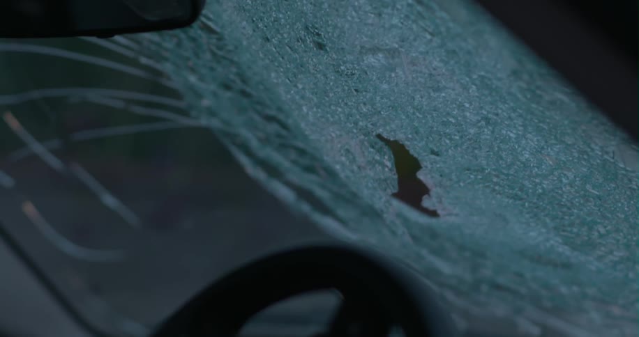 A person bashes in the windshield of a car