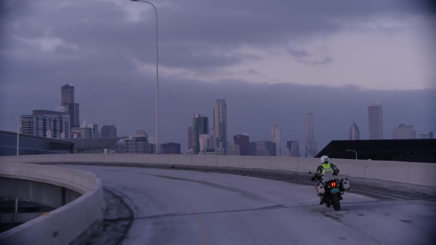 A motorcyclist rides on a city highway at sunset