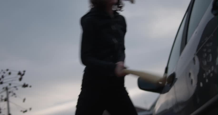 A young woman beats a car with a bat
