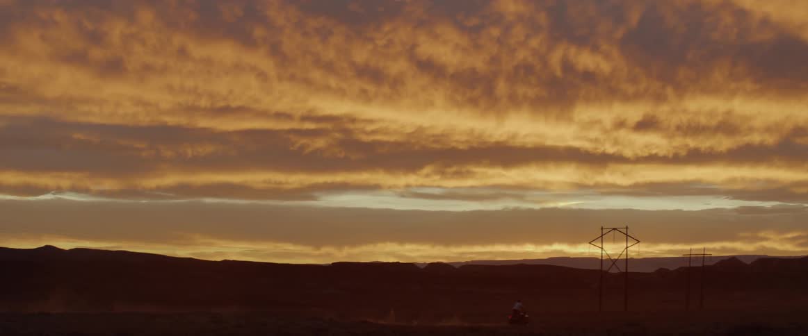Motorcycle drives through a desert at sunrise