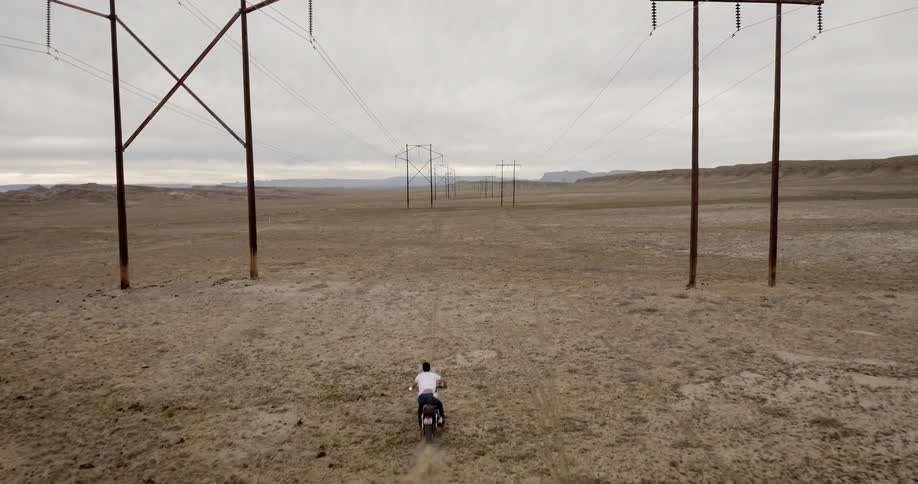 A man rides a motorcycle in the desert under power lines