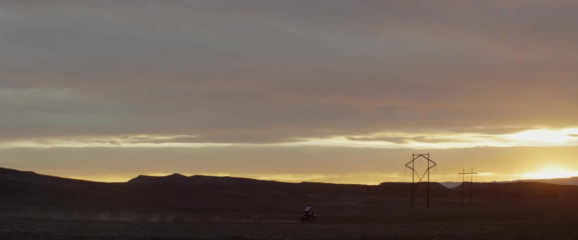Someone is riding a motorcycle through the desert at sunset
