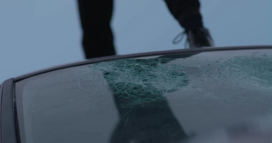 A woman smashes a car windshield with a baseball bat