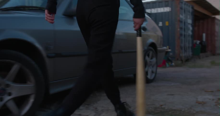 Woman swings a baseball bat in her hand while walking by a car