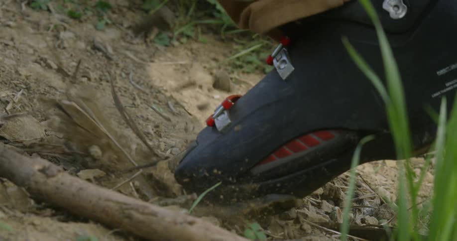 A person wearing ski boots is hiking up a dirt path during the day