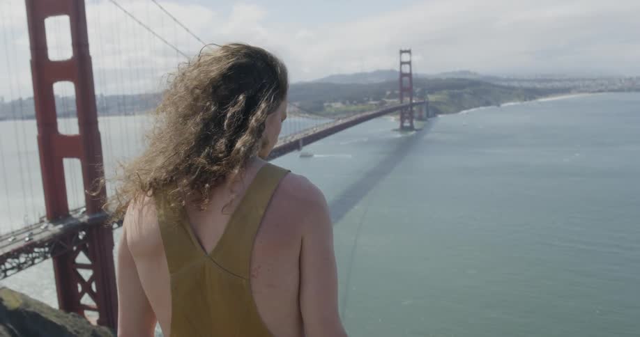 A man stands on a ridge looking down at the golden gate bridge