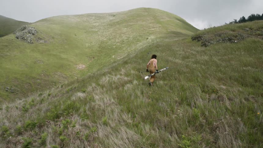 Man walking up a grassy hill on windy day