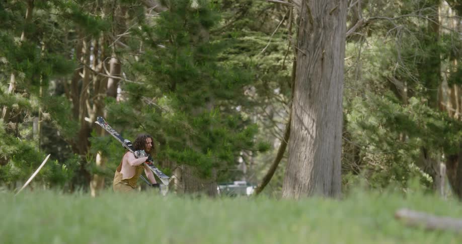 A man carries skis and poles through the grass
