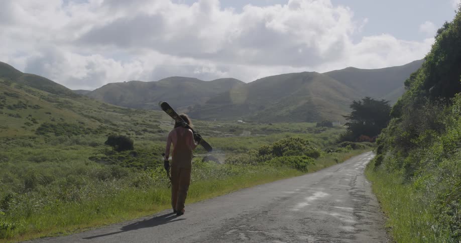 A man carries skis down a narrow mountain road