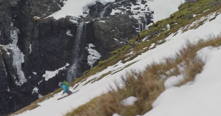 A professional skier skis down the mountain in front of waterfall