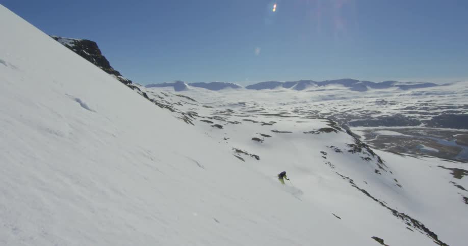 A person skis down a mountain slope on a sunny day