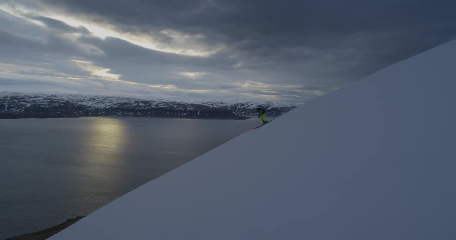 A person skis down the snowy hill towards the ocean