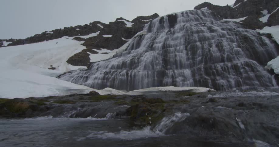 A wide but shallow water fall is flowing down some rocks into a small stream