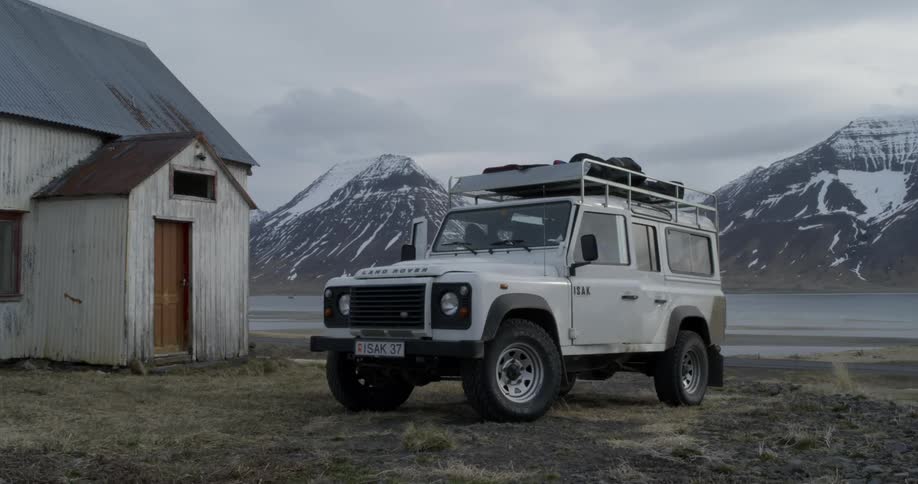 People exit a white jeep that is parked outside of a building with a mountain range behind them
