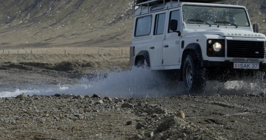 A land rover drives through a wild river with lots of spray