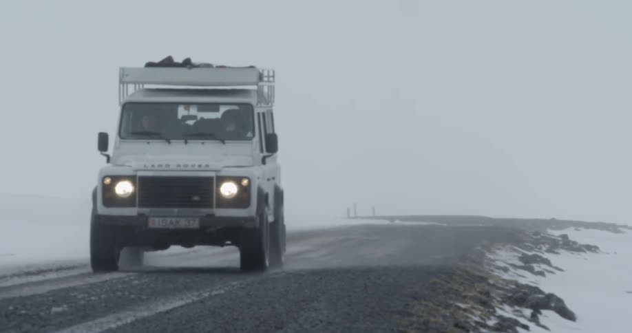 Person driving jeep on road surrounded by snow on the ground
