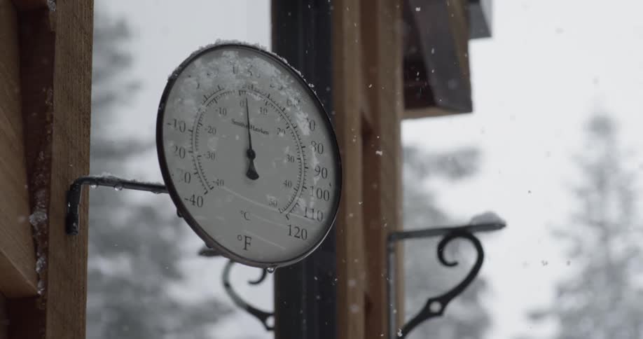 A thermometer is attached to the side of a building while it's snowing out