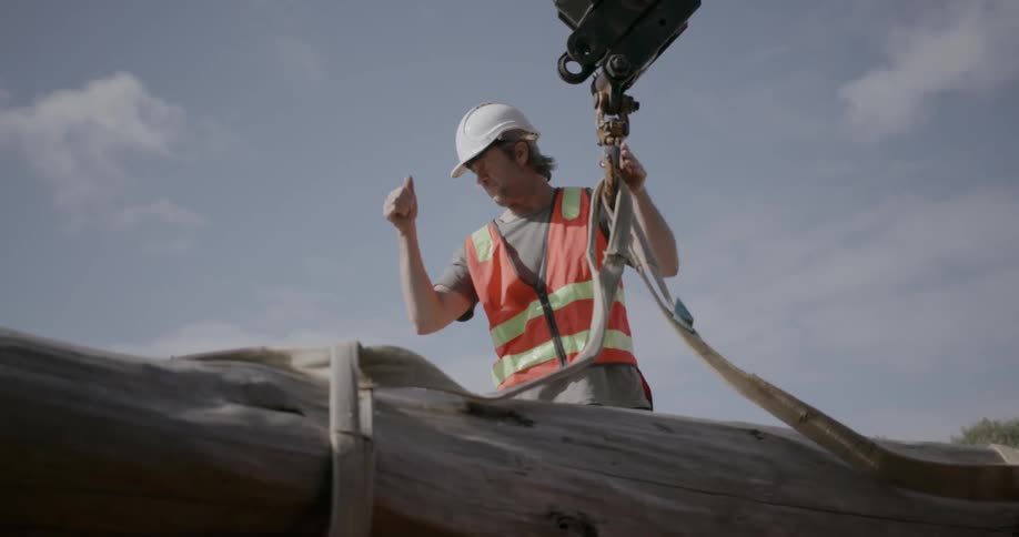 A man hooks straps onto the crane hook then gives a thumbs up